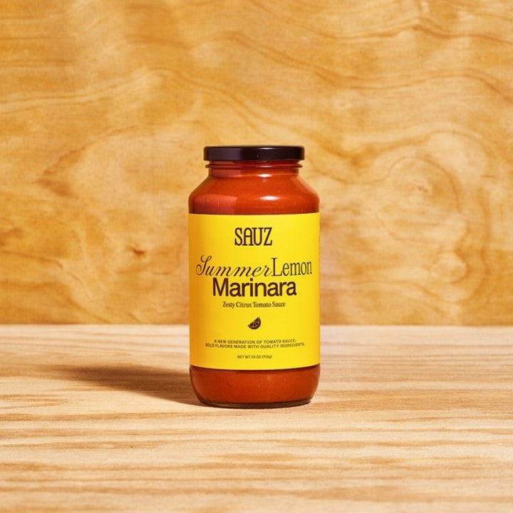 Sauz Summer Lemon Marinara in a glass jar with a bright yellow label, set against a warm wood background. This zesty, citrus-infused tomato sauce is light, bold, and made with locally-sourced ingredients. Perfect for pasta, seafood, and fresh, summery dishes.