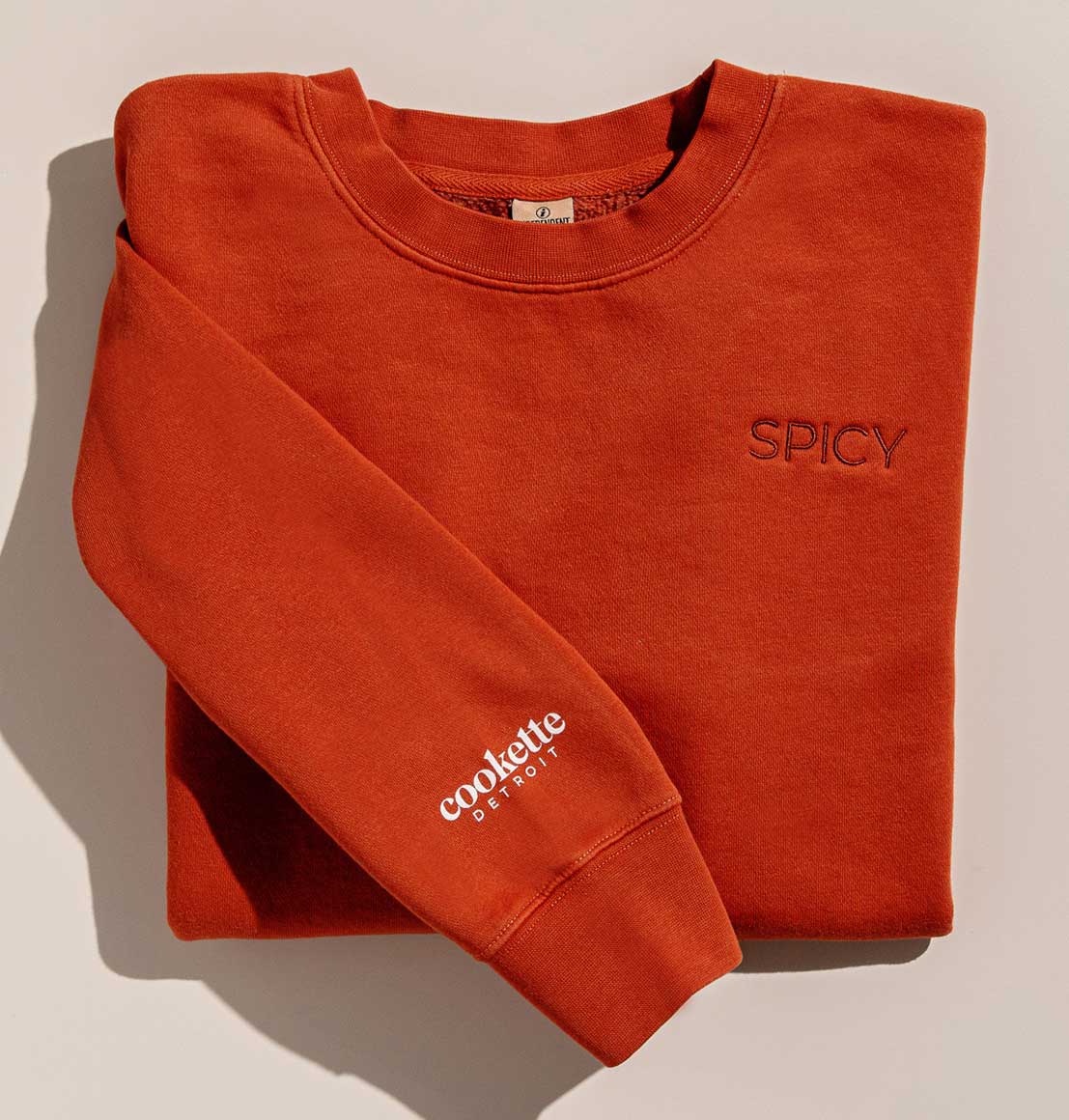Incredibly cozy sweatshirt with the word "spicy" embroidered on the left size of the chest. The Cookette Detroit logo is screenprinted on the sleeve in white. Both the sweatshirt and embroidered word are in a burnt orange/chili pepper color.